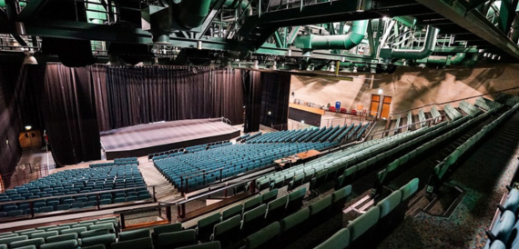 Wide view of the auditorium's teal seating beneath exposed rigging