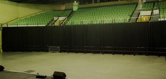 Empty arena with tiered green seating and a black stage curtain