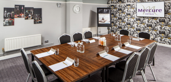 Boardroom with a wooden table, black chairs and a Mercure Hotels screen.