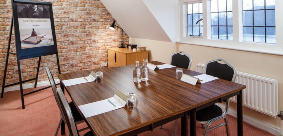 Meeting room with a wooden table, black chairs and an exposed brick wall.