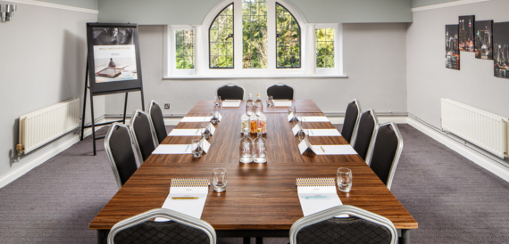 Boardroom with a long wooden table, black chairs and framed pictures on the wall.