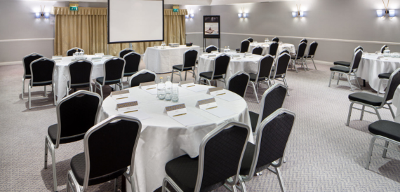 Meeting room with round tables, black chairs and a projector screen.