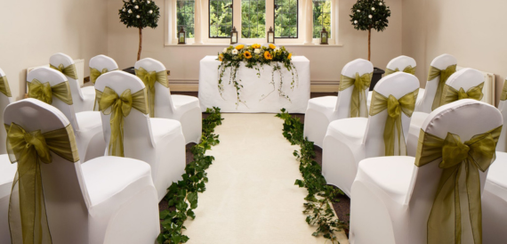 Wedding ceremony aisle with white chair covers, gold sashes and topiary trees.