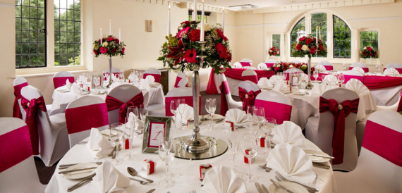 Banqueting room set with white chair covers, red sashes and tall floral centrepieces.
