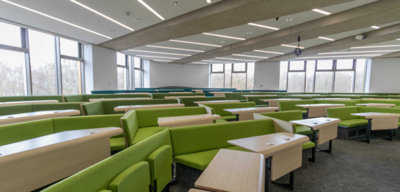 Lecture theatre with green bench seating and fold-down desks by large windows