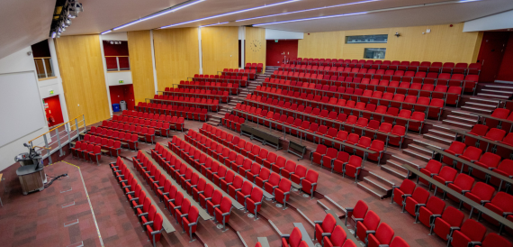 Tiered lecture theatre with rows of red seats facing the front stage