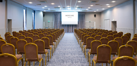 Conference room set theatre-style with rows of gold chairs facing a screen.