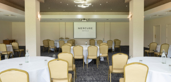 Conference room with round tables, gold chairs and a projector screen.