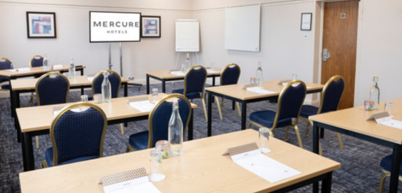 Meeting room set classroom-style with navy chairs facing a wall screen.