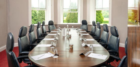 Boardroom with a long table, black leather chairs and garden views.