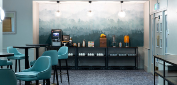 Self-service coffee bar with teal stools set against a forest-mural wall.