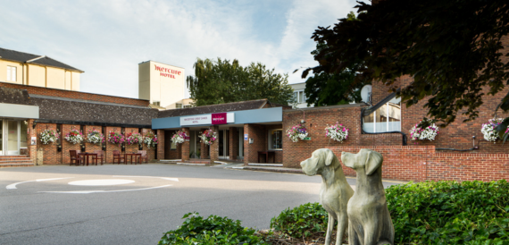 Hotel entrance with hanging flower baskets, signage and dog statues by the driveway.