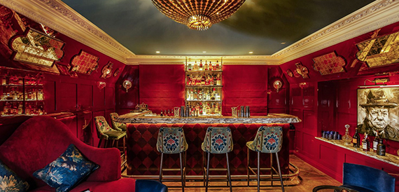 Red bar room with an ornate chandelier and patterned bar stools