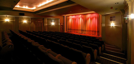 Cinema auditorium with red seats facing a red-curtained stage