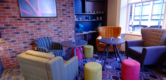 Lounge with orange armchairs, a brick wall and colourful stools