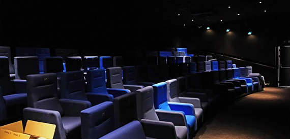 Empty screening room with blue-lit seats and a storage crate on the floor
