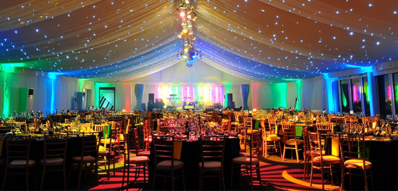 Marquee party with colourful lighting, round dining tables and guests in evening wear