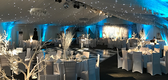 Marquee decorated for a winter event with blue lighting, white chair covers and a dance floor