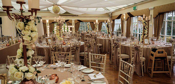 Wedding reception room with round tables, gold linen and tall rose candelabra centrepieces.