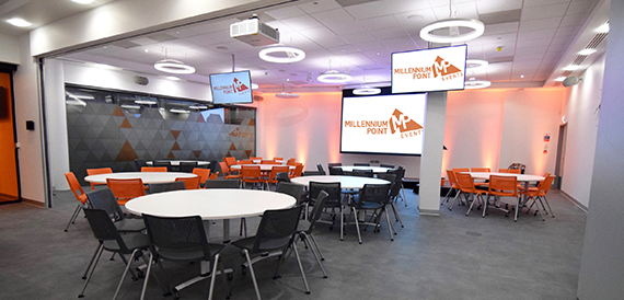 Breakout space with round tables, orange chairs and coloured wall lighting.