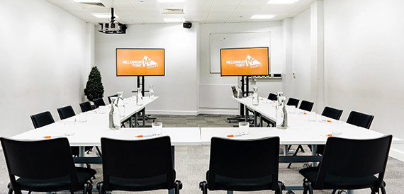 Meeting room set cabaret-style with black chairs facing two wall-mounted screens.