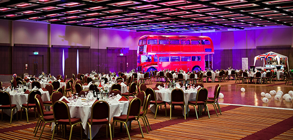 Gala dinner room with round tables and a red double-decker bus display