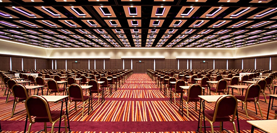 Vast conference hall set classroom-style with rows of desks under patterned ceiling lights