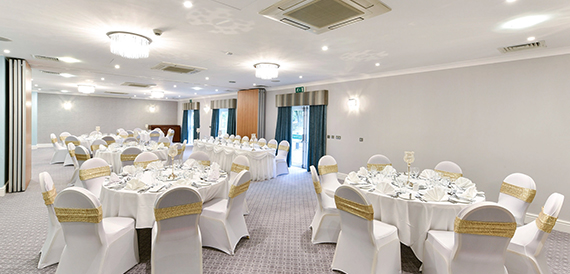 Banqueting room set for a wedding with white chair covers, gold sashes and round tables.