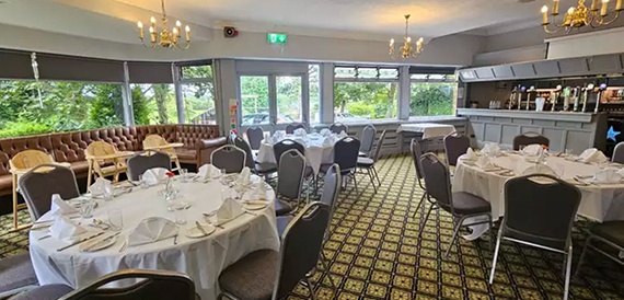 Function room set for dining with round tables, chandeliers and a bar area.