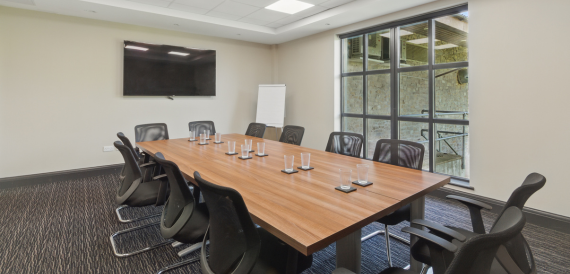 Boardroom with a long wood table, black chairs and a wall-mounted screen
