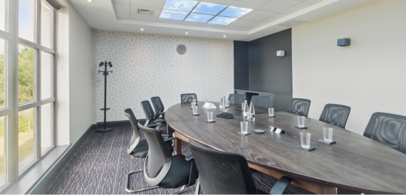 Boardroom with an oval wood table, black chairs and a skylight