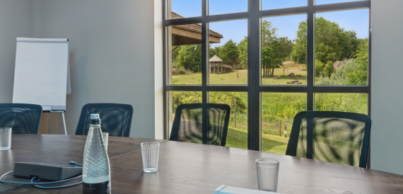 Boardroom table with water glasses beside a window overlooking parkland