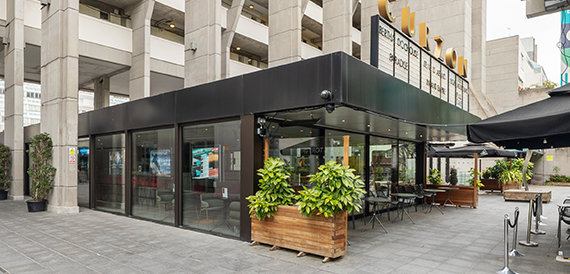 Cinema exterior with glass frontage, potted plants and outdoor seating
