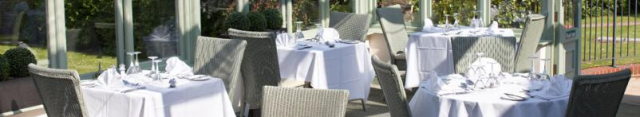 Outdoor dining table set with a white cloth and wicker chairs in the garden.