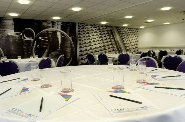 Round conference table set with glasses, notepads and pencils in front of an industrial mural