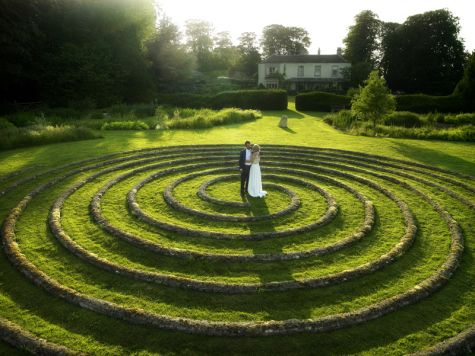 Bride and groom embracing at the centre of a circular stone maze on the lawn