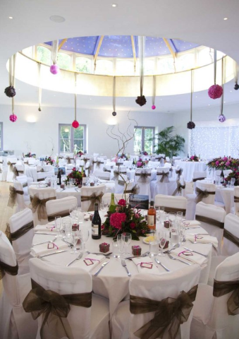 Domed conservatory dining room set for a wedding with round tables and chair sashes