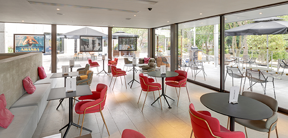 Bar area with red chairs, round tables and glass walls to a terrace
