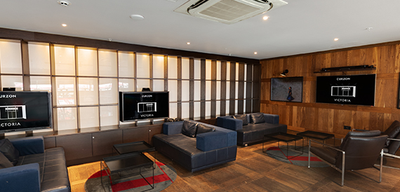 Lounge with wood panelling, dark sofas and wall-mounted screens