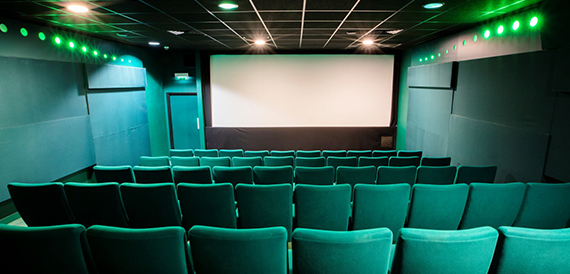 Cinema auditorium with teal seats beneath a row of green lights
