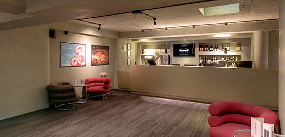 Bar counter with shelves of bottles and red curved armchairs