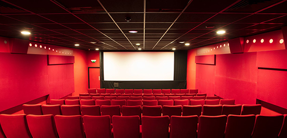 Cinema auditorium with red seats facing a bright screen