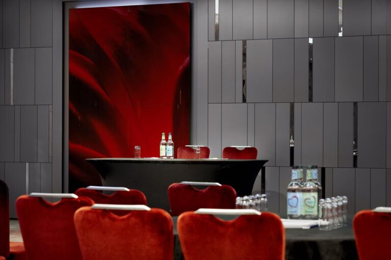 Close-up of a round table with water bottles, red velvet chairs and a red abstract artwork.
