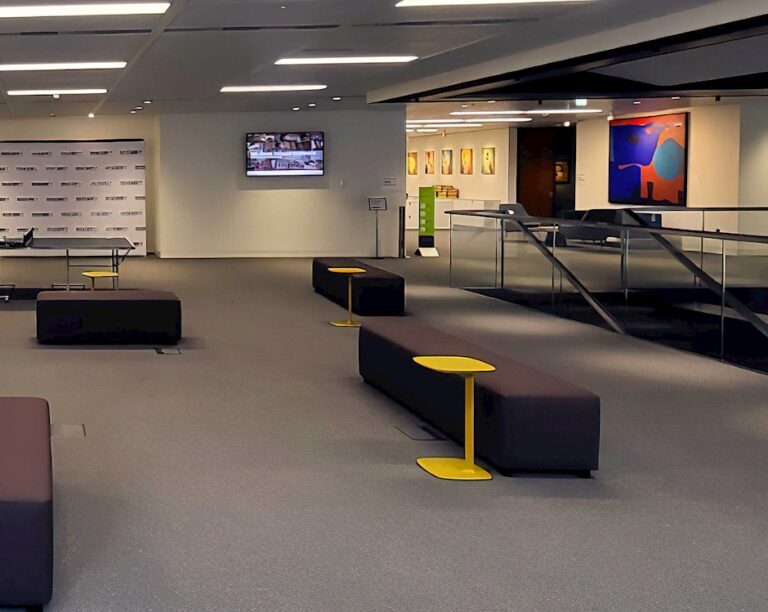 Collaboration Forum with high stools, yellow tables and a wall-mounted screen