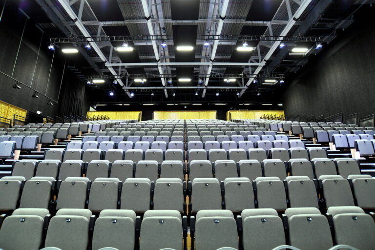 Large auditorium with tiered rows of grey seating and stage lighting rig