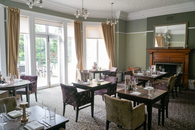 Dining room with small tables, a period fireplace and garden view
