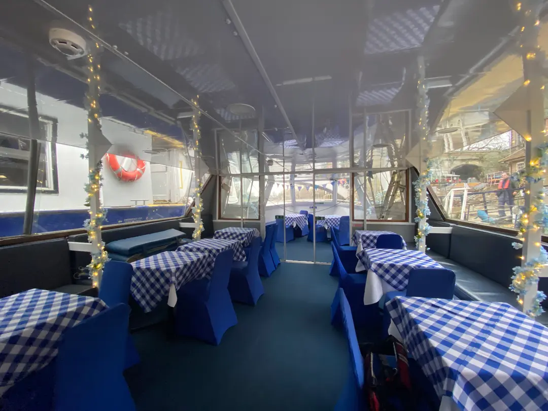 Dining saloon with blue-checked tablecloths, string lights and a lifebuoy on the wall
