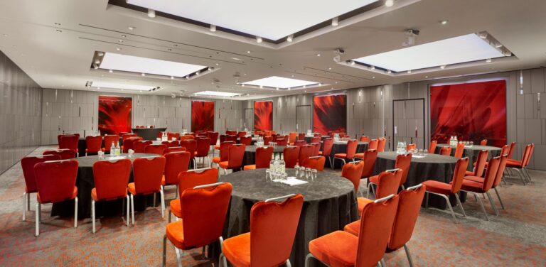Cabaret-style event space with round tables, orange velvet chairs and red abstract art panels.