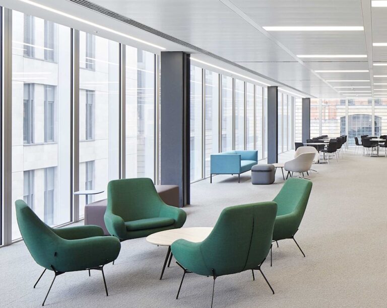 First floor lounge with green armchairs and round tables by floor-to-ceiling windows