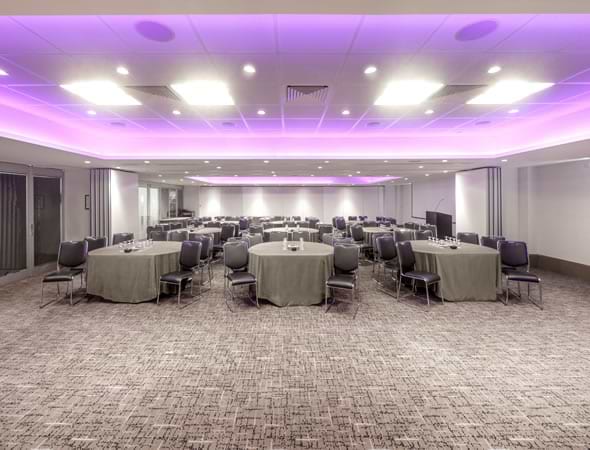Meeting room set cabaret-style with round tables under purple lighting